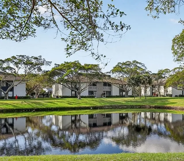Serene apartment complex with lush green lawns and a tranquil pond, surrounded by beautiful tree-lined pathways.