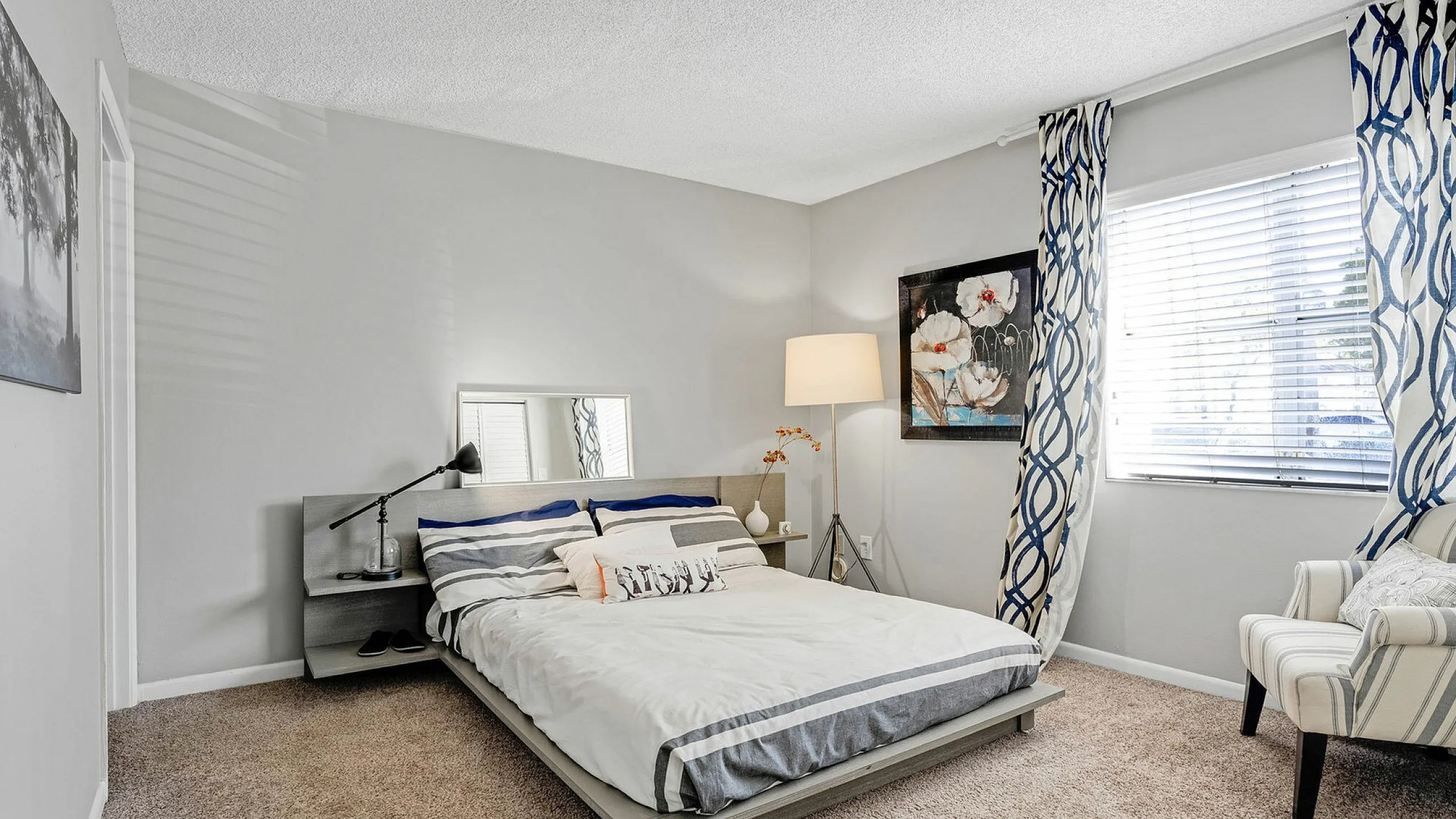 Inviting bedroom with plush carpeting, modern gray bed, and stylish decor bathed in natural light.