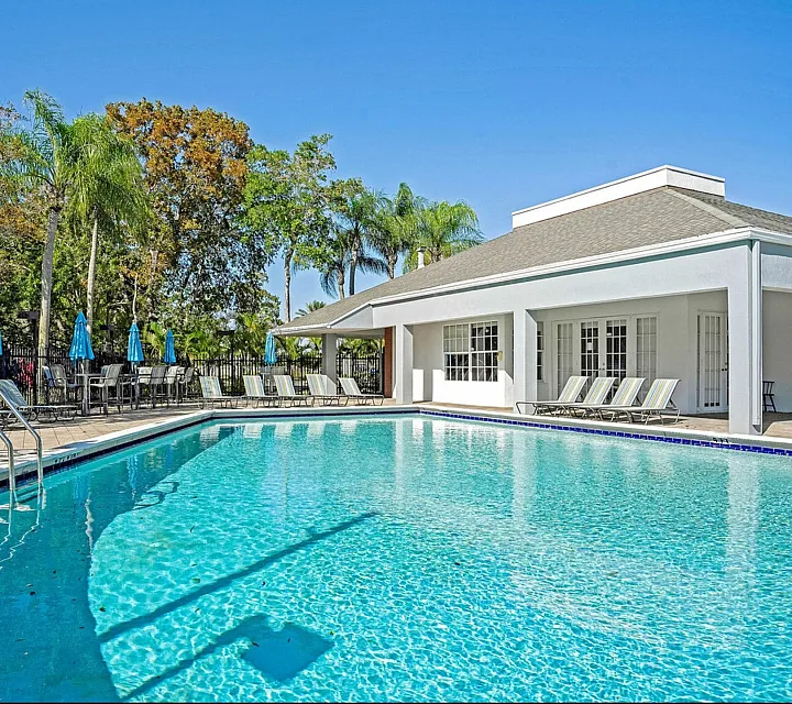 Inviting outdoor pool area with crystal-clear water and sun loungers, surrounded by lush green palm trees and vibrant blue umbrellas.