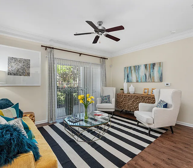 Chic living room with a cozy sofa, stylish armchairs, geometric glass coffee table, and sliding doors opening to a vibrant garden view.