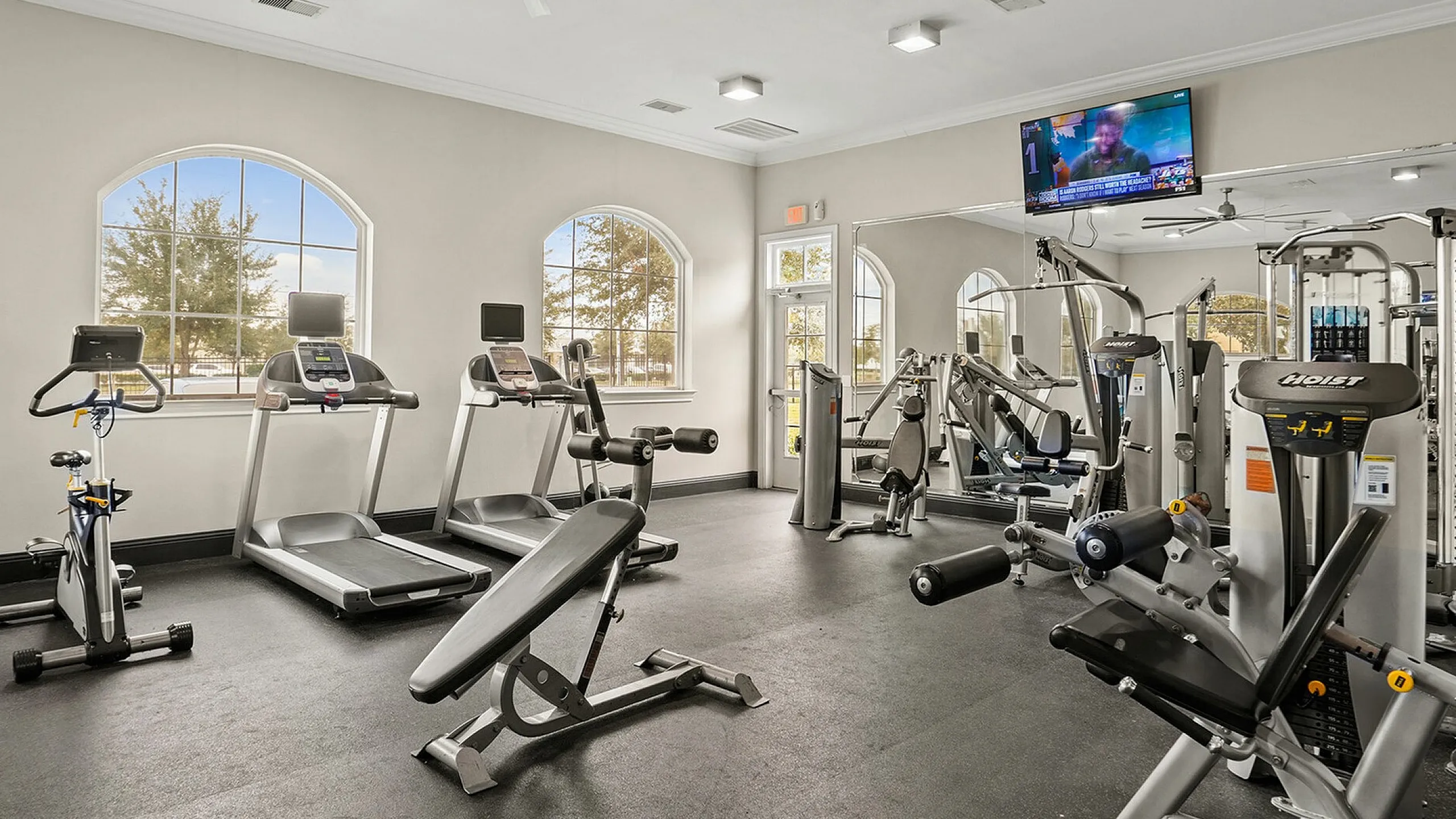 Bright and modern apartment gym with high ceilings, featuring treadmills, weight machines, and outdoor views.