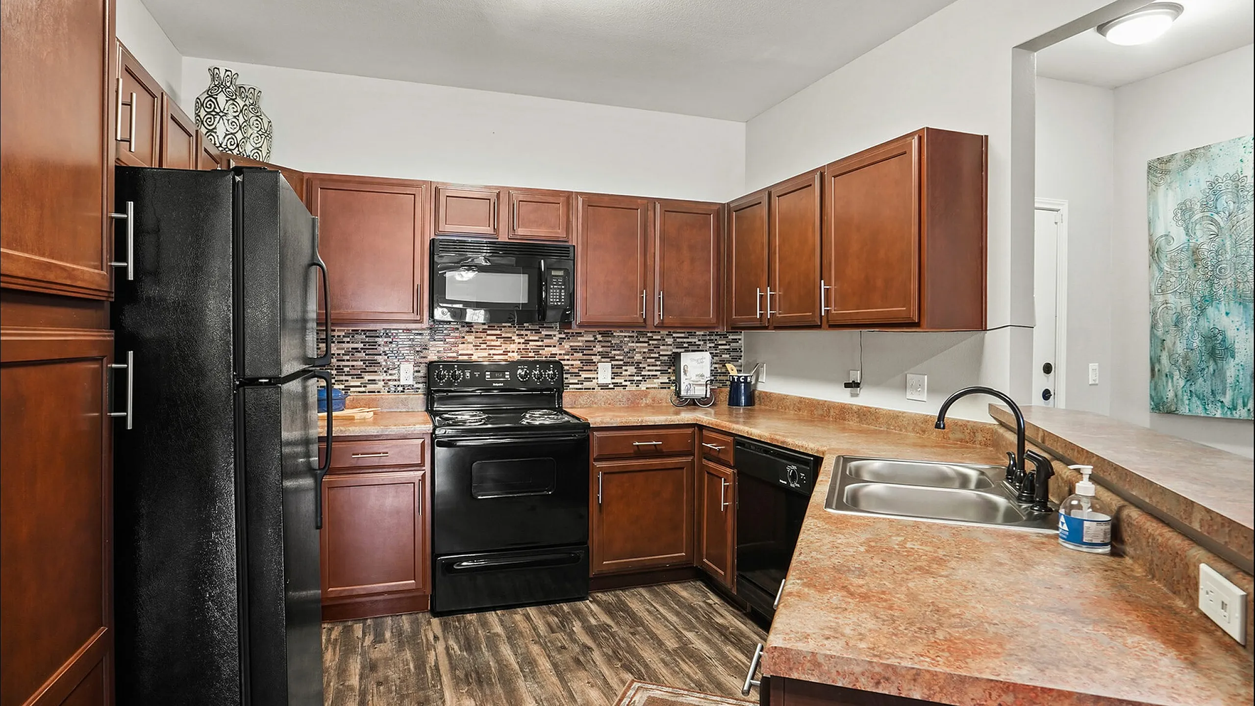 Modern kitchen with rich wood cabinetry, sleek black appliances, and stylish backsplash accent in a spacious layout.