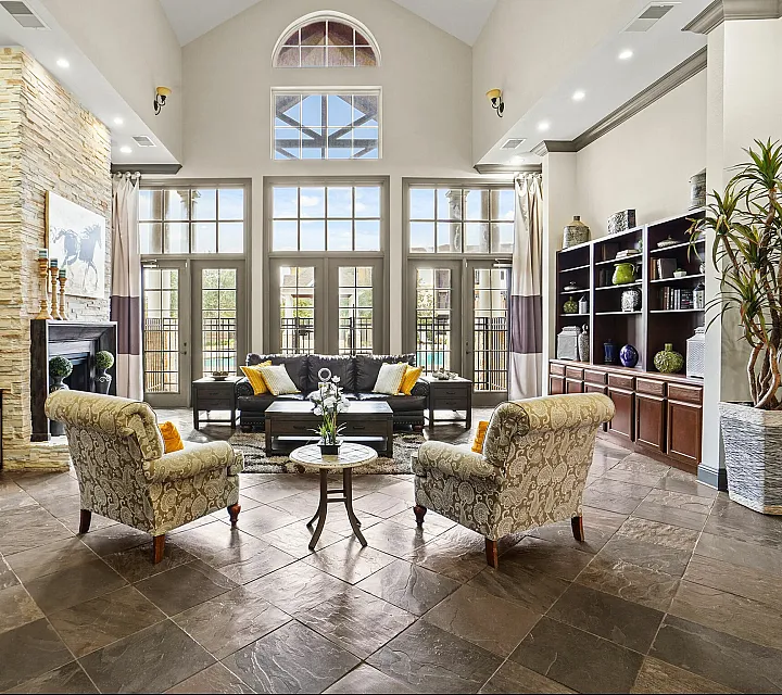 Elegant living room with high ceilings, stone fireplace, and large windows offering natural light; features cozy seating and modern decor.
