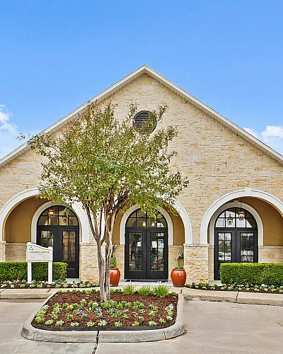 Charming stone building with arched windows, surrounded by manicured landscaping and set against a clear blue sky.