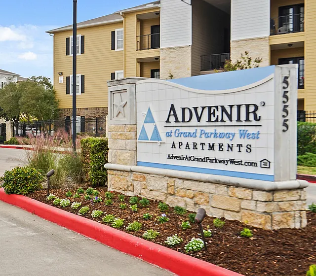 Inviting entrance of Advenir at Grand Parkway West Apartments, featuring modern architecture, lush landscaping, and a welcoming driveway.