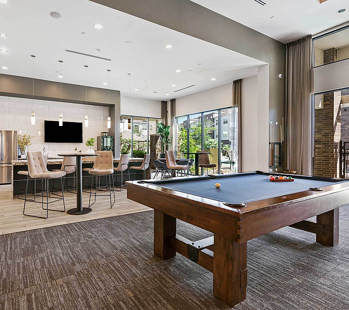 Luxurious apartment lounge featuring a modern kitchen with high chairs, elegant lighting, and a sleek billiards table for entertainment.
