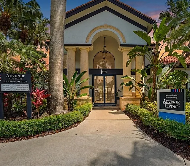 Elegant leasing office entrance with grand columns surrounded by lush tropical landscaping at sunset.