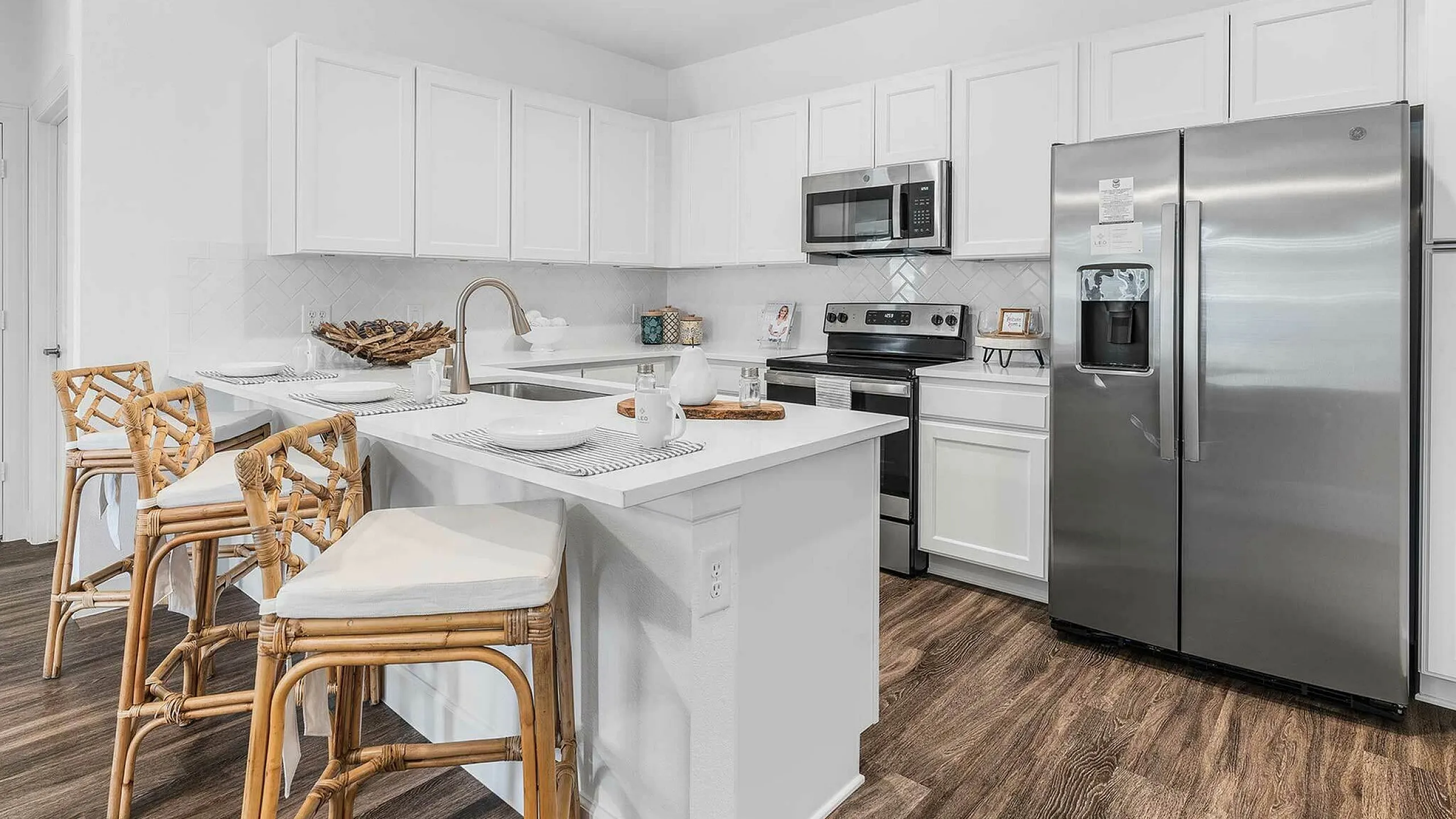 Modern kitchen with sleek white cabinets, stainless steel appliances, and a stylish island with wicker barstools.