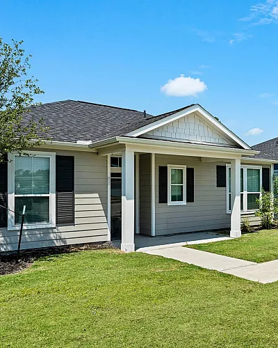 Charming row of modern single-story homes with inviting front porches and well-maintained lawns under a bright blue sky.