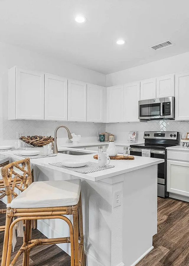 Modern kitchen with sleek stainless steel appliances, elegant white cabinetry, and cozy breakfast bar accented by natural wood barstools.