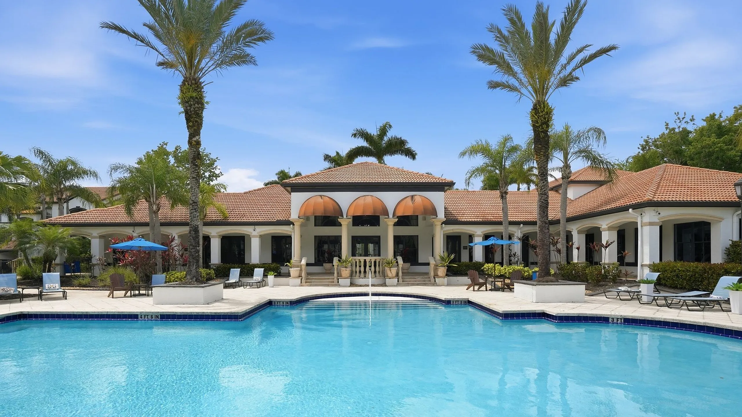 Luxurious resort-style outdoor pool area with elegant architecture, surrounded by palm trees and inviting lounge chairs under a clear blue sky.