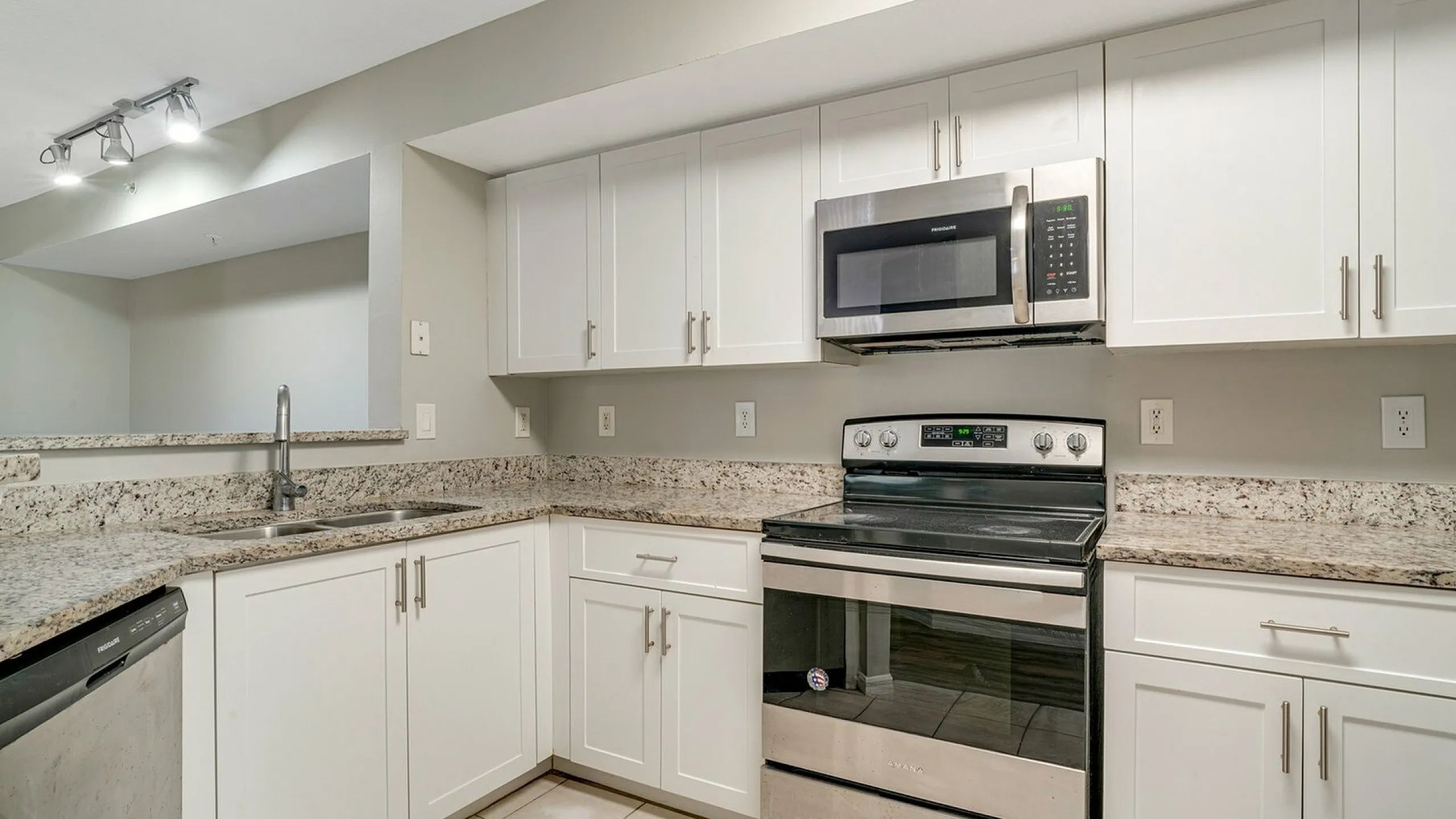 Modern kitchen with sleek stainless steel appliances, elegant granite countertops, and pristine white cabinetry.