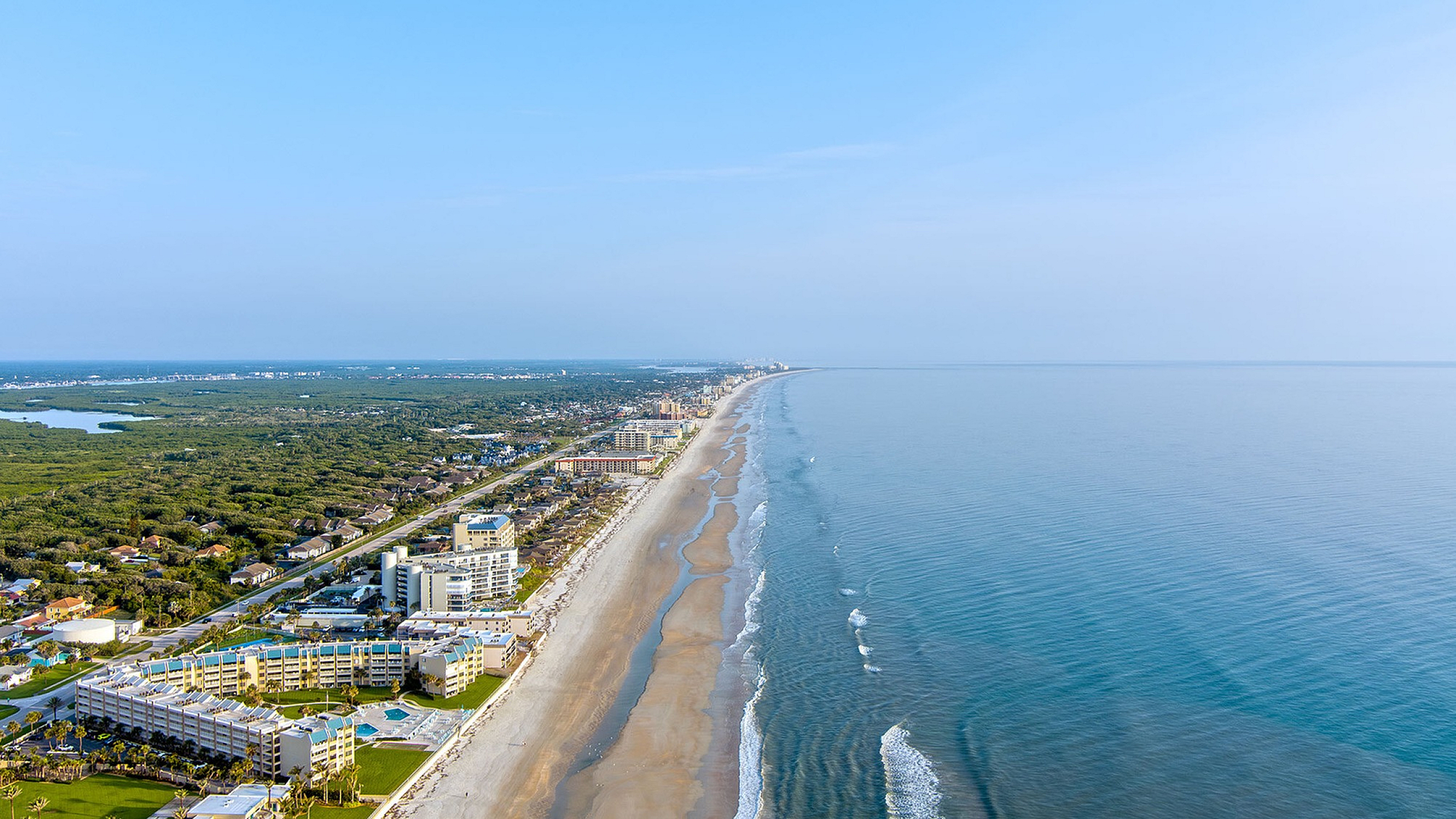 Stunning aerial view of a serene coastline with luxurious beachfront resorts and lush greenery, offering an idyllic seaside living experience.
