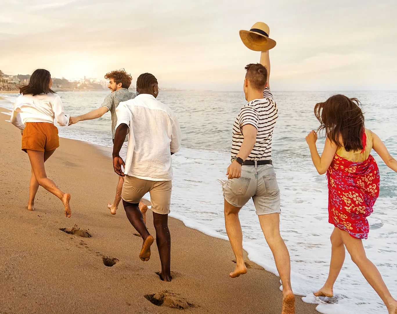 Joyful friends running along the beach at sunset, capturing moments of fun and freedom by the ocean.