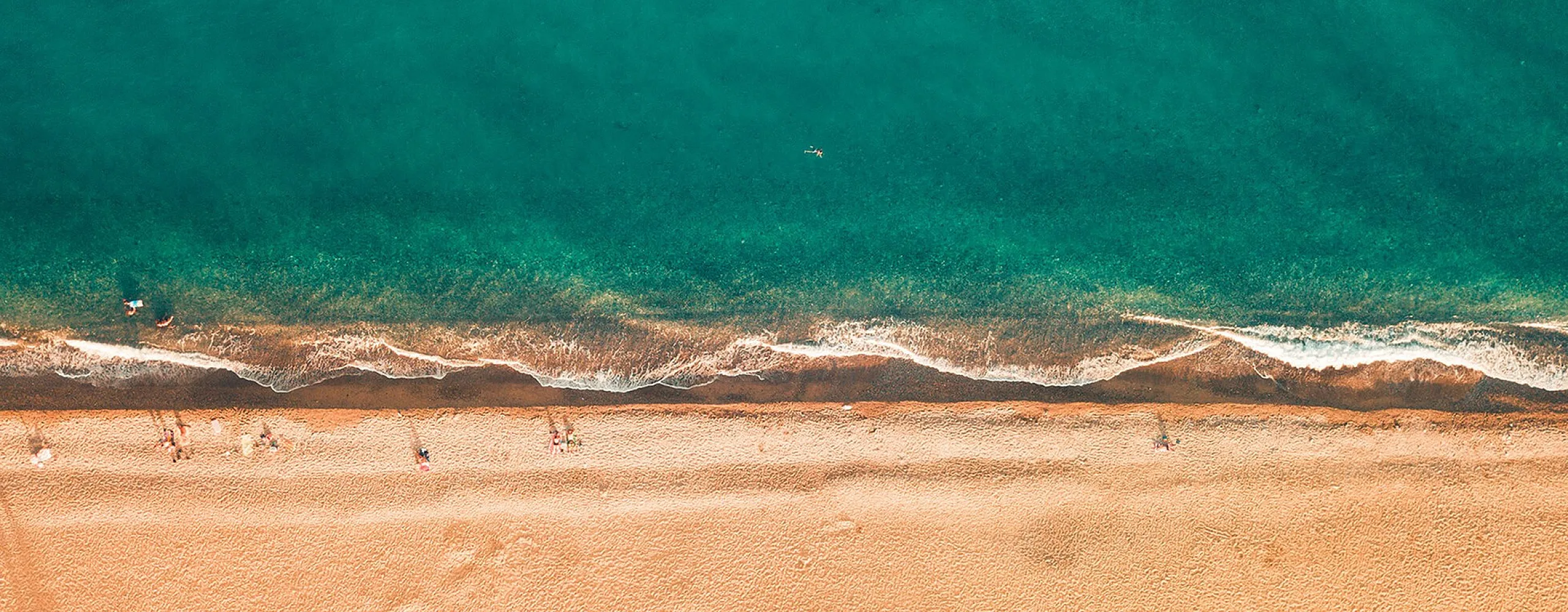 Aerial view of a pristine beach with golden sand and turquoise waves, evoking a tranquil coastal paradise.