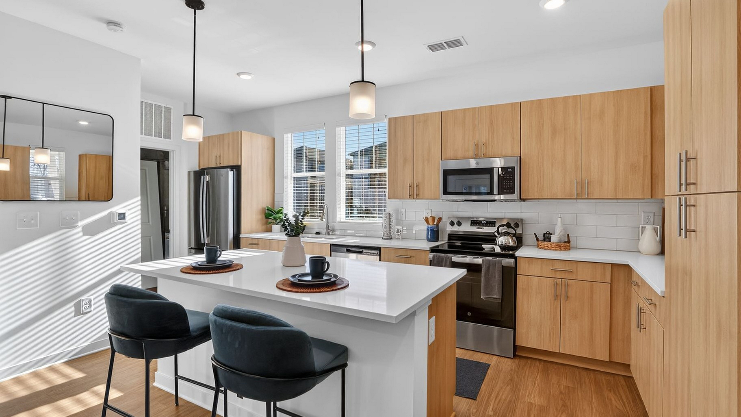 Modern kitchen with sleek white countertops, light wood cabinetry, stainless steel appliances, and stylish pendant lighting, showcasing an inviting and functional space.