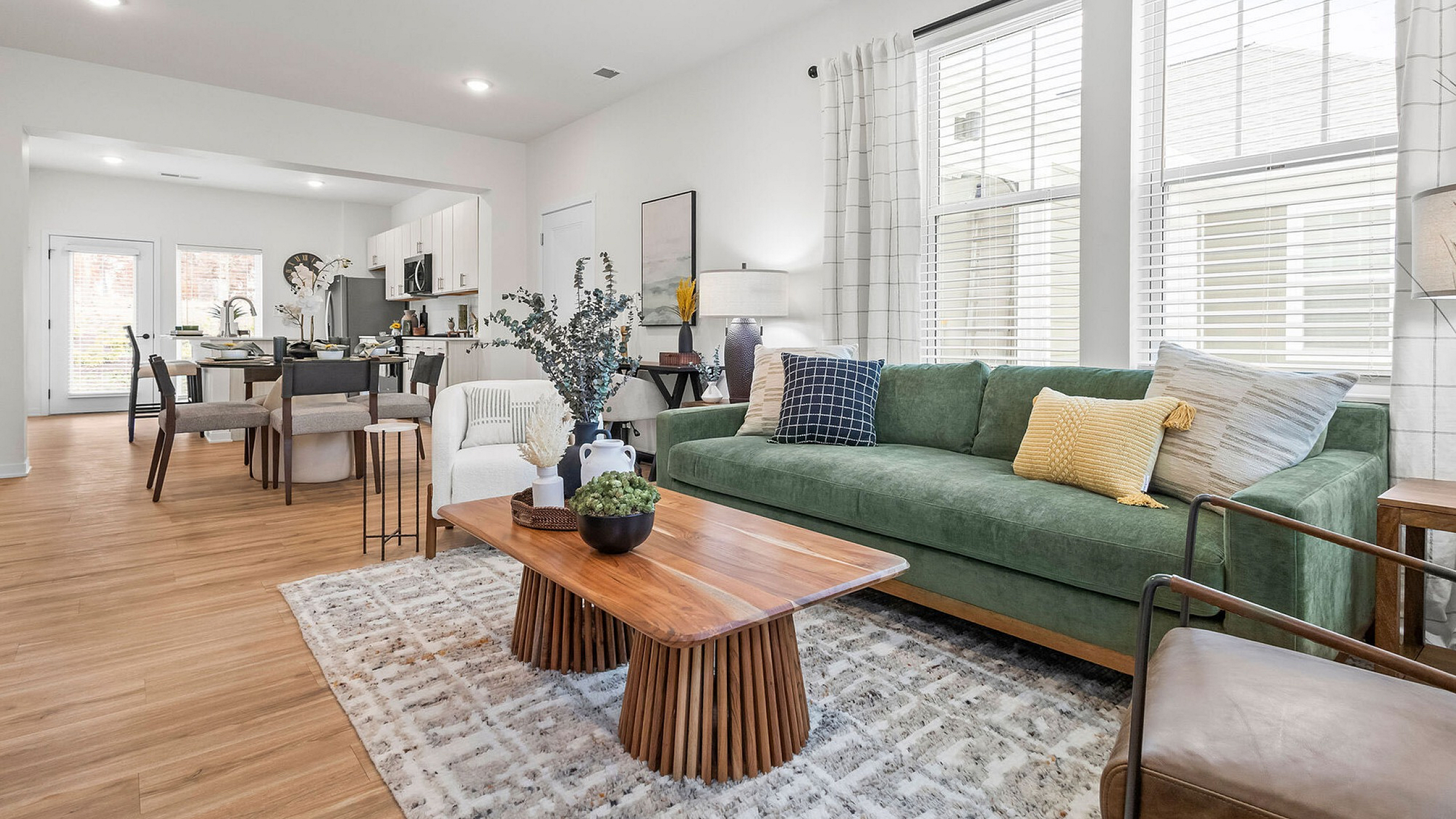 Bright, open-concept living space featuring a luxurious green sofa, elegant dining area, and modern kitchen with natural light streaming through large windows.