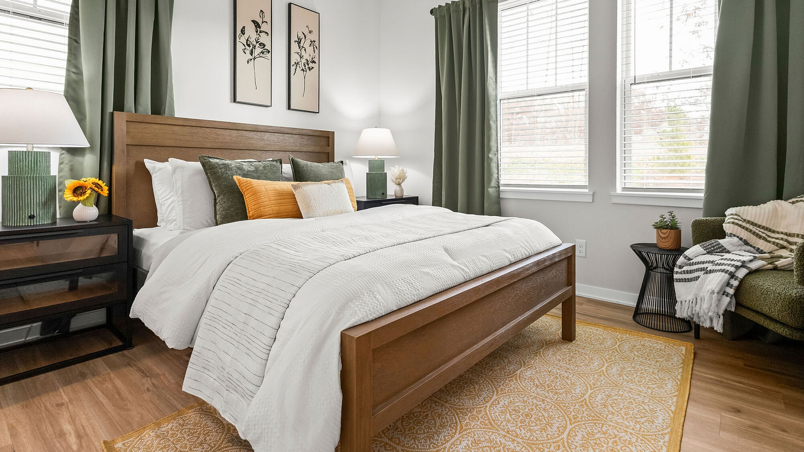 Inviting bedroom with a cozy wooden bed frame, plush pillows, stylish decor, and abundant natural light from large windows with green curtains.