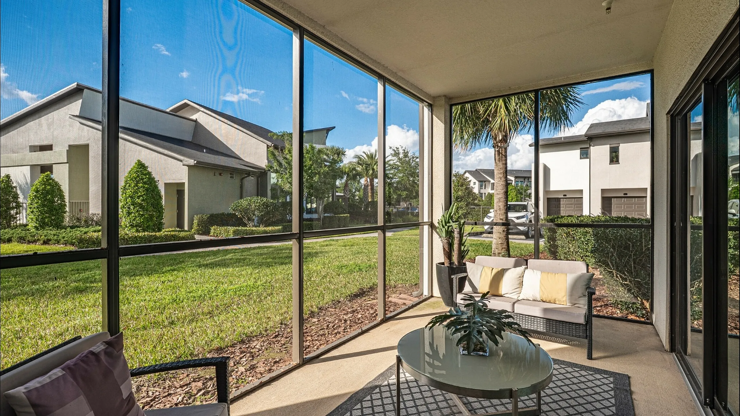 Charming screened-in patio with modern seating overlooking lush green landscaping and contemporary architecture, perfect for relaxation and enjoying the serene view.