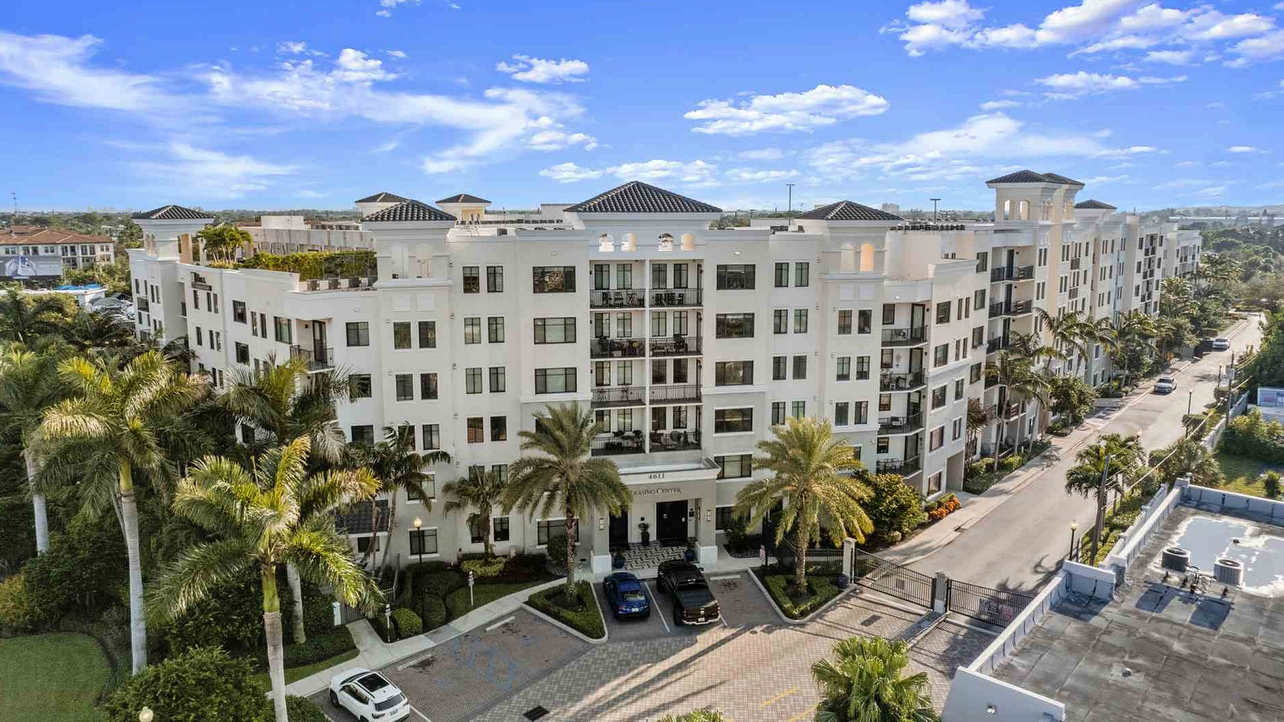Luxurious apartment building with palm-lined entrance, elegant balconies, and lush greenery under a clear blue sky.