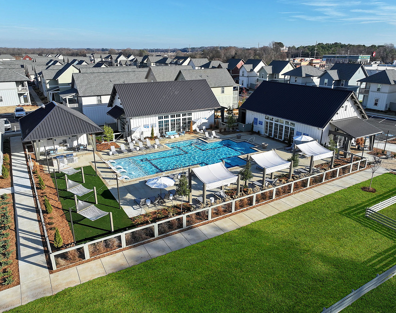 Charming community view highlighting a modern outdoor pool area with cozy hammocks and elegant lounging spaces, set amidst a backdrop of stylish homes.