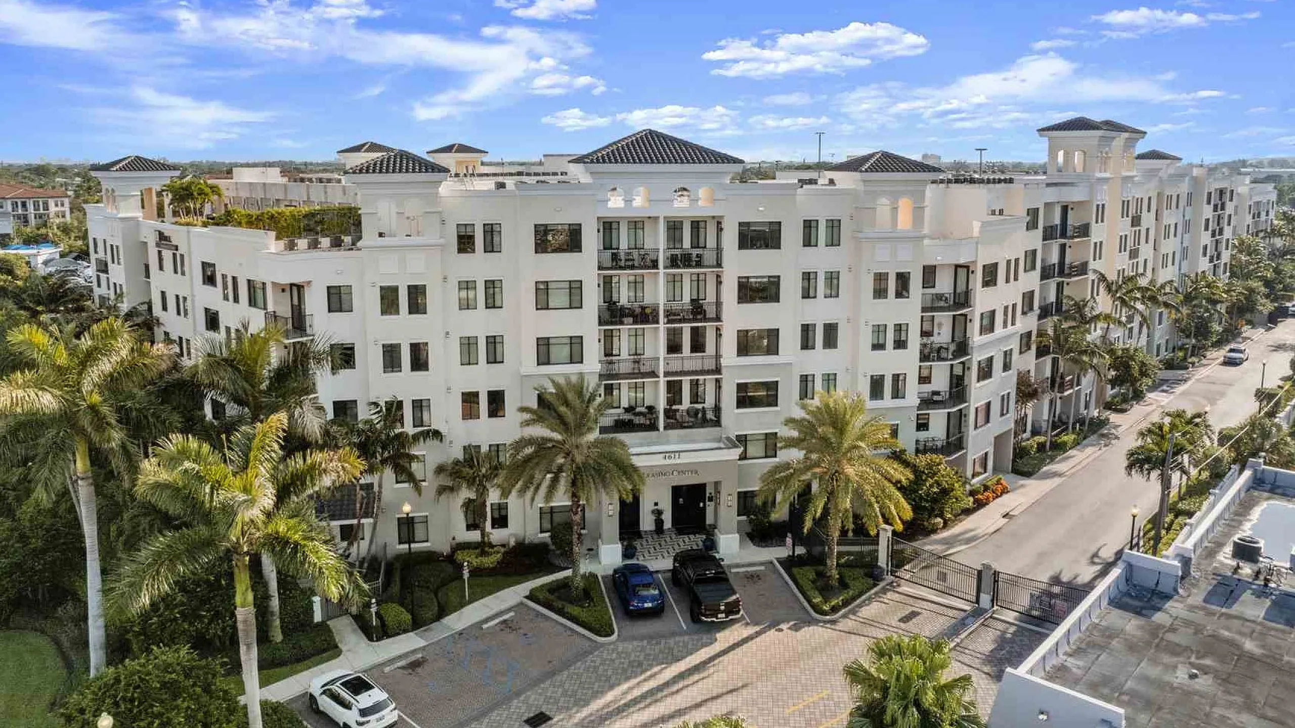 Modern white apartment complex with elegant architecture, surrounded by lush palm trees and clear blue skies.
