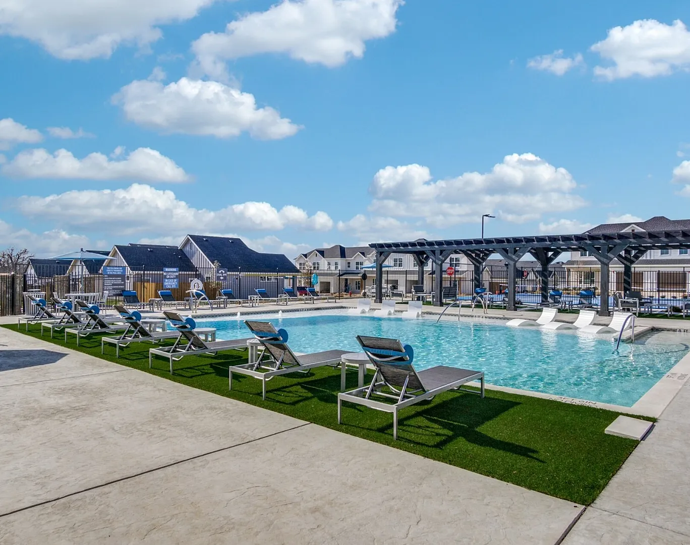 Inviting outdoor swimming pool area with stylish lounge chairs and a pergola under a bright, sunny sky in a modern residential community.