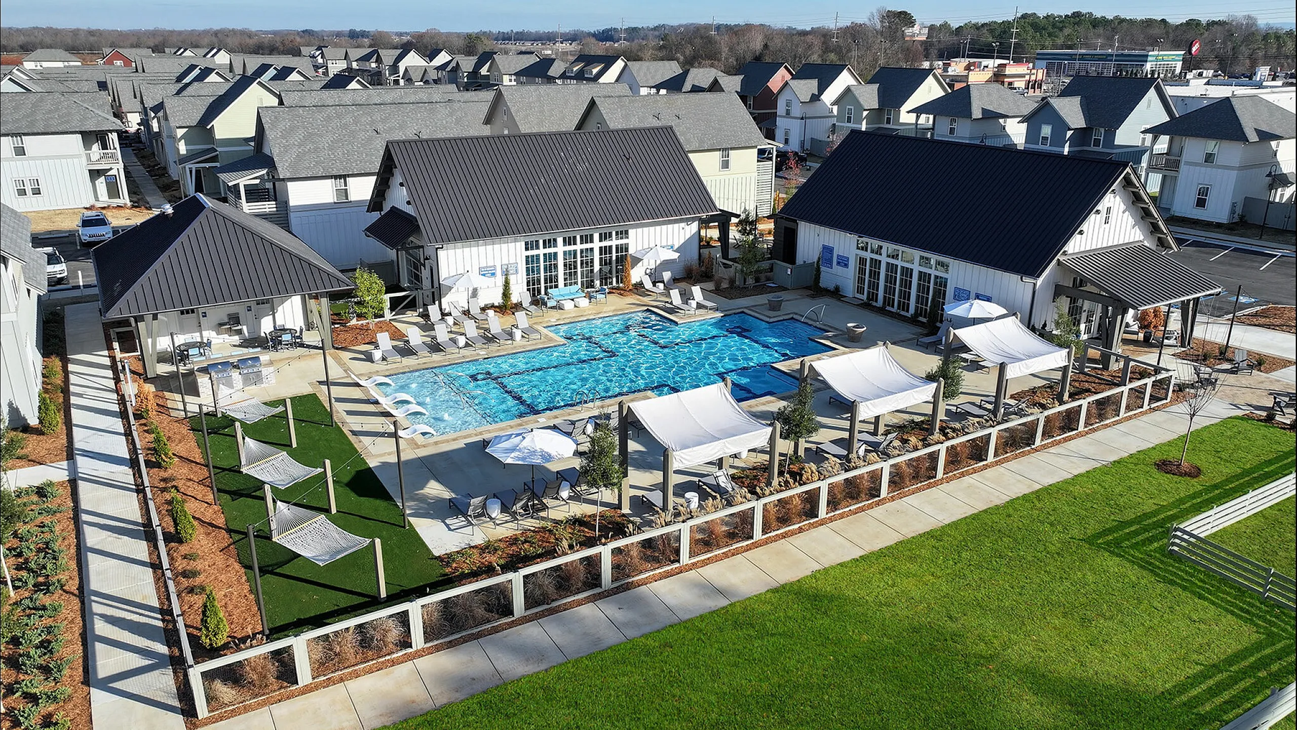 Luxurious apartment complex featuring a sparkling outdoor pool, shaded lounge areas, and lush green landscaping.