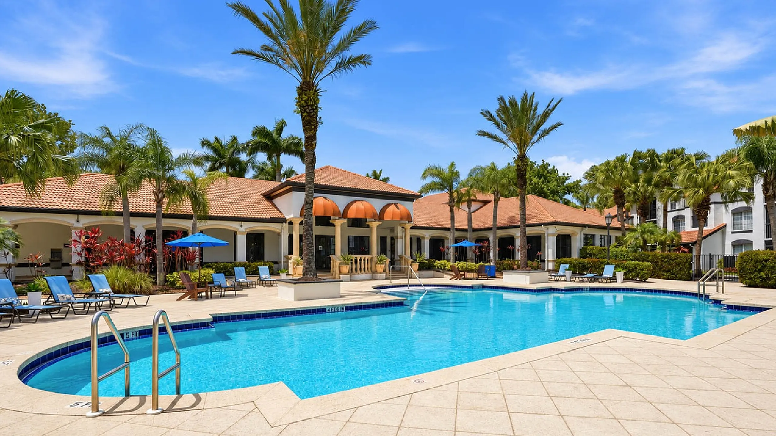 Luxurious apartment complex with a pristine outdoor pool, surrounded by palm trees and elegant lounge chairs, offering a serene resort-style ambiance.