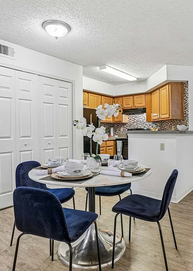 Chic apartment interior featuring a cozy dining area with elegant blue chairs, a modern kitchen with warm wood cabinetry, and stylish decor, highlighting a sophisticated blend of comfort and style.