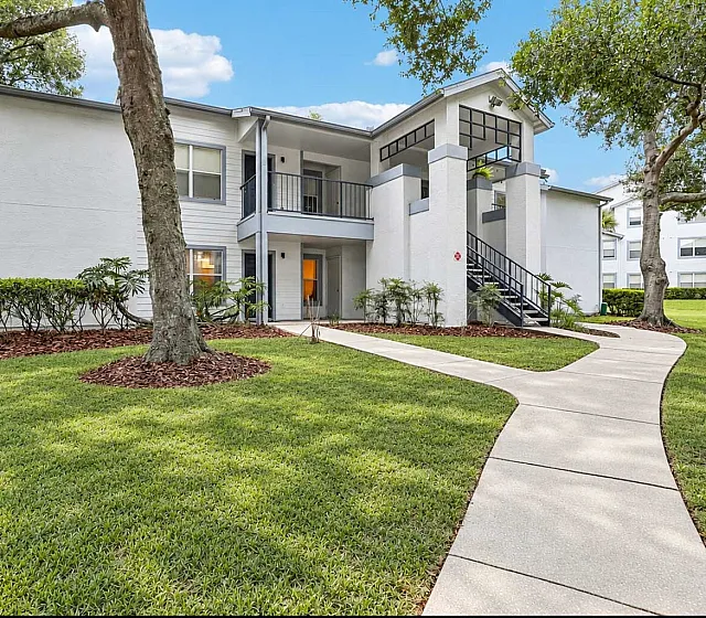 Charming two-story apartment building with a modern facade, surrounded by lush greenery and a winding pathway.