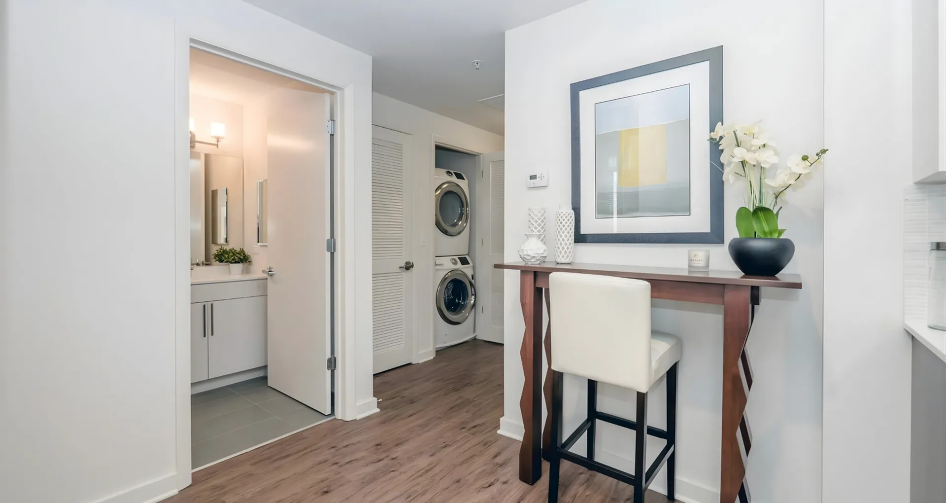 Modern apartment entryway featuring elegant wooden flooring, stylish bar seating, and a chic laundry area with stacked washer and dryer.