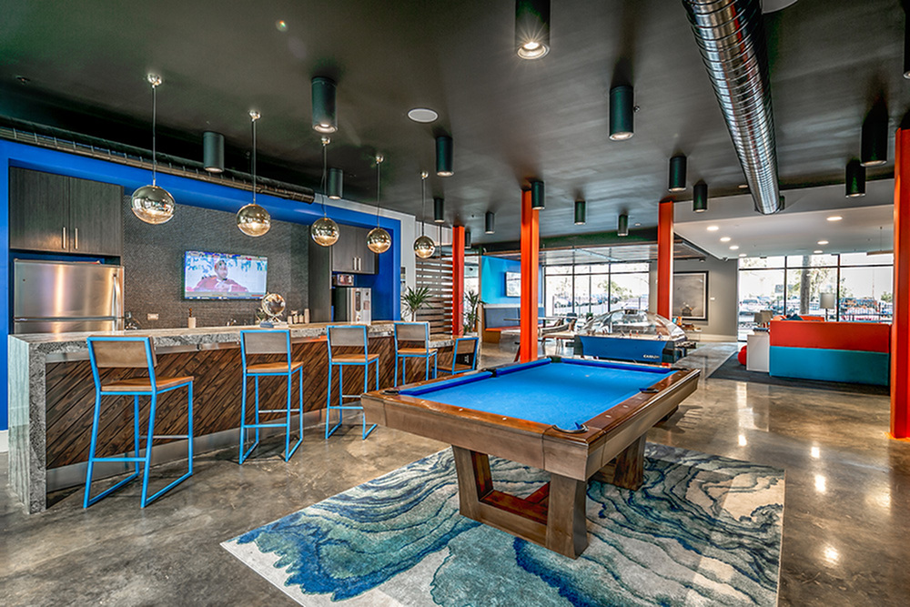 Modern apartment lounge featuring a sleek bar area, vibrant lighting, and a stylish pool table for relaxed social gatherings.