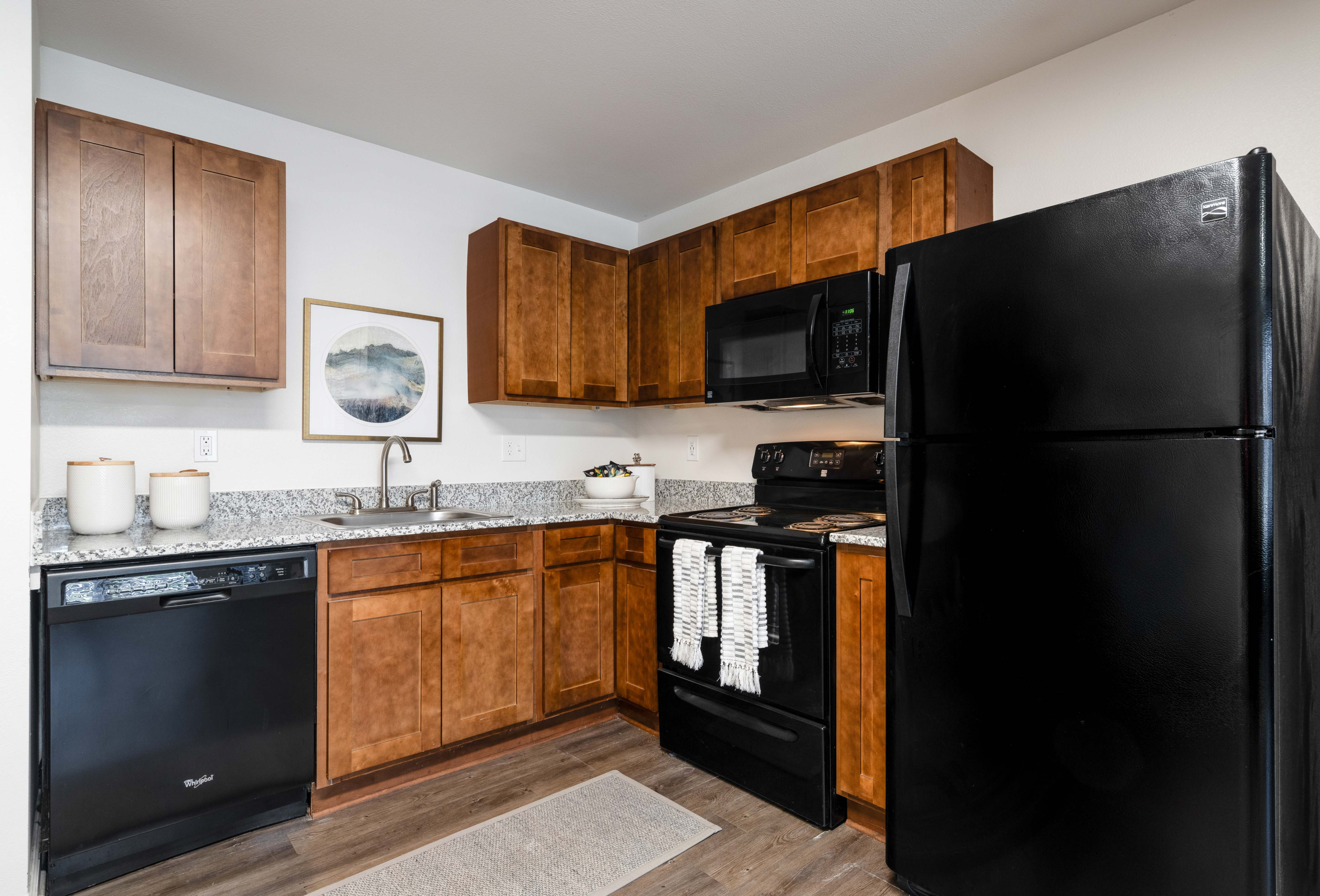 Model apartment kitchen with brown cabinets and black appliances