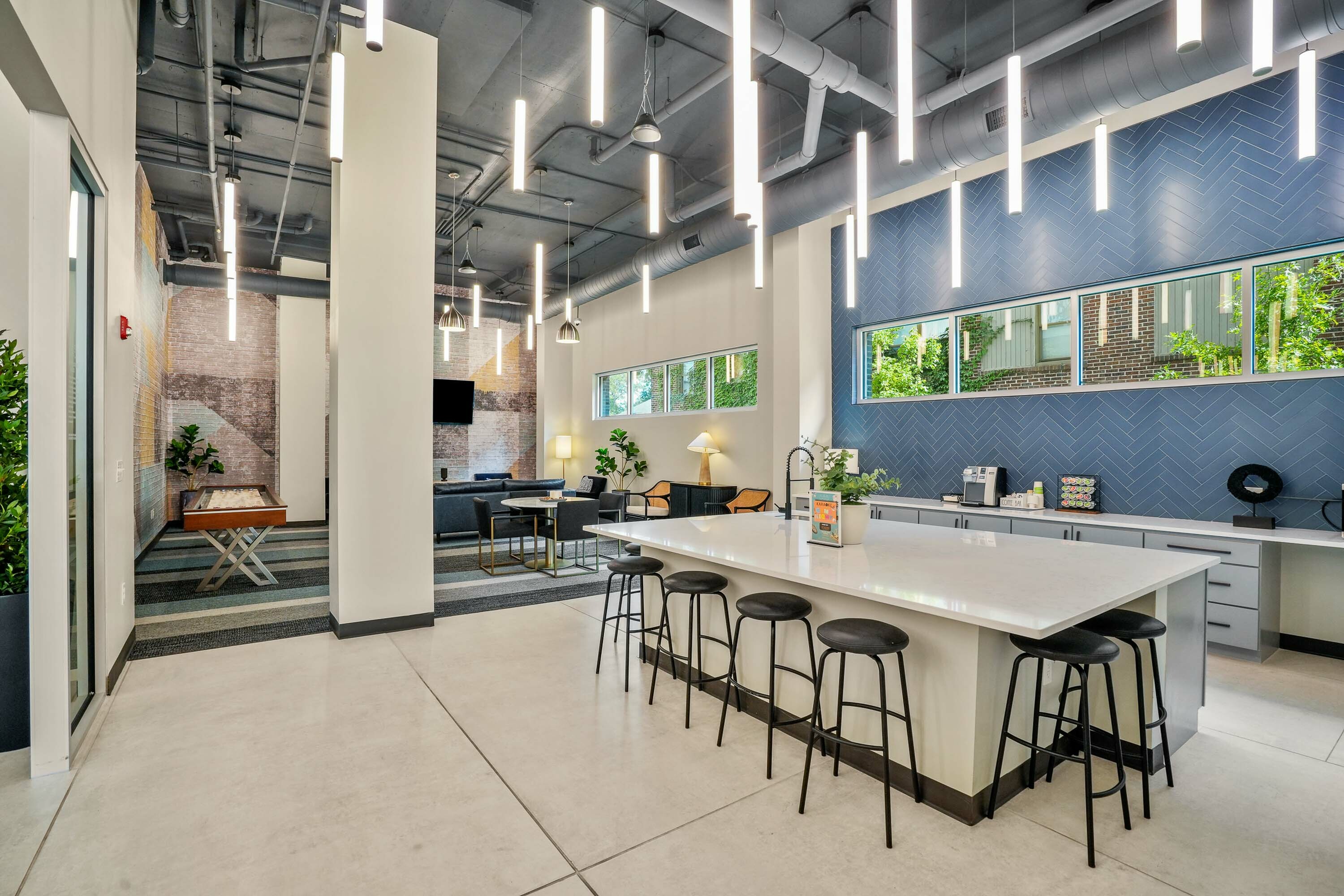 Modern lounge area featuring chic lighting, a spacious kitchen island with stools, and stylish seating in a vibrant, open-concept community space.