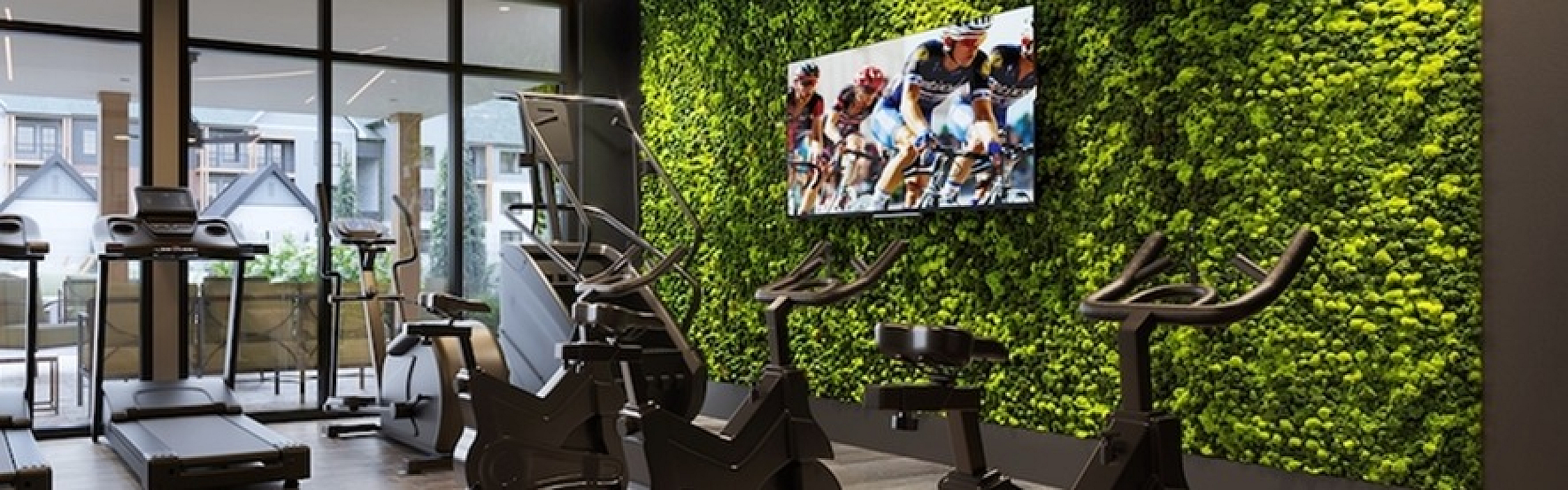 Modern fitness center with treadmills, stationary bikes, and a lush green wall.