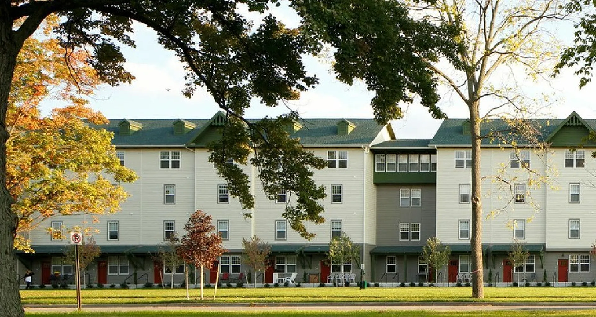 Charming suburban apartment building with green roofs, surrounded by trees and a public road in the foreground.