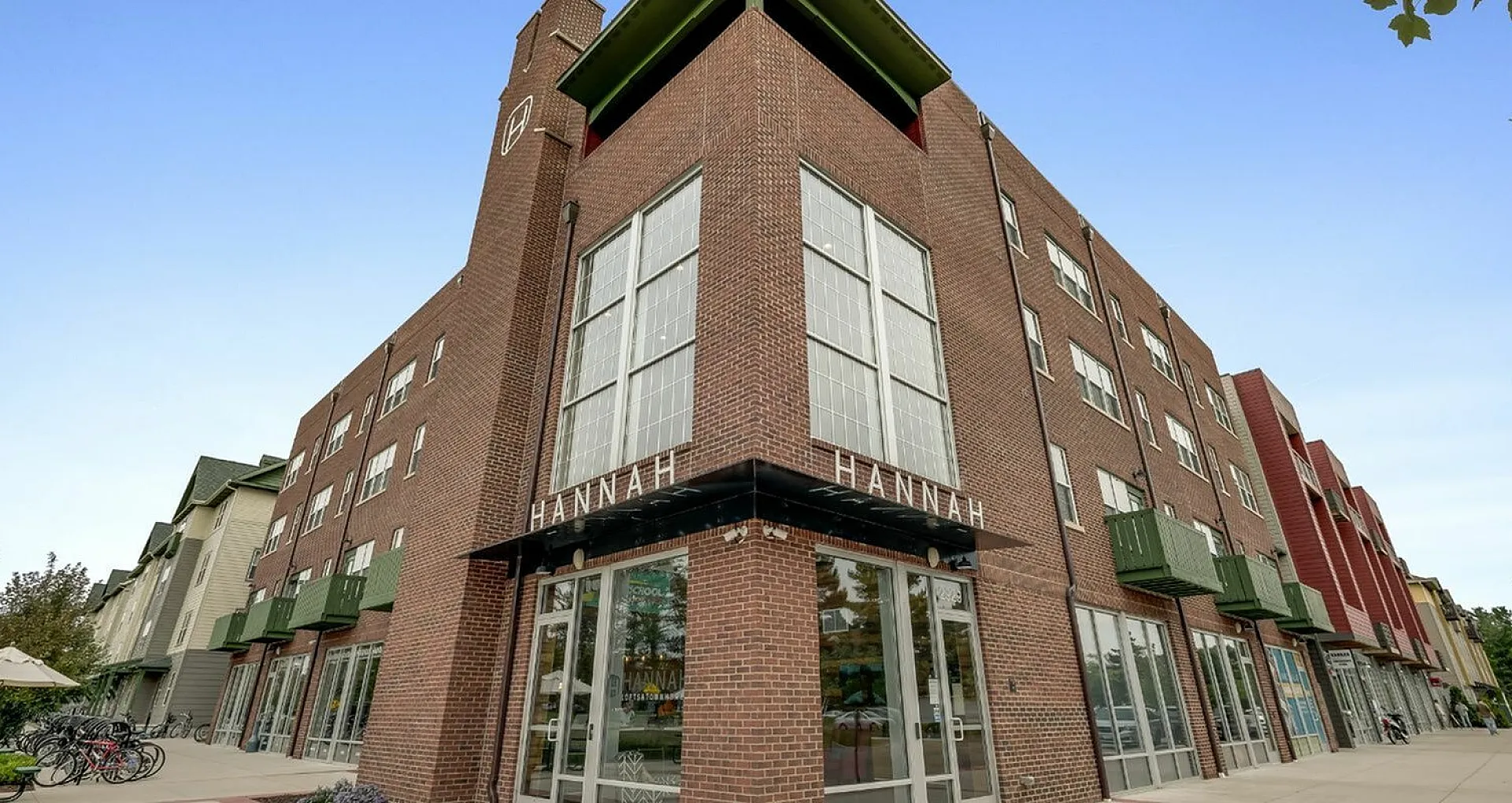 Modern four-story brick apartment building with large corner windows and green balconies.