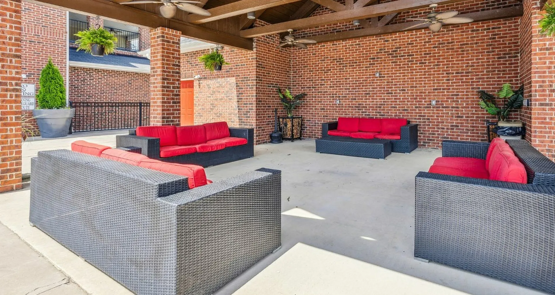 Inviting outdoor lounge area with modern wicker sofas and vibrant red cushions, under a stylish wood beam ceiling, perfect for relaxing and entertaining.