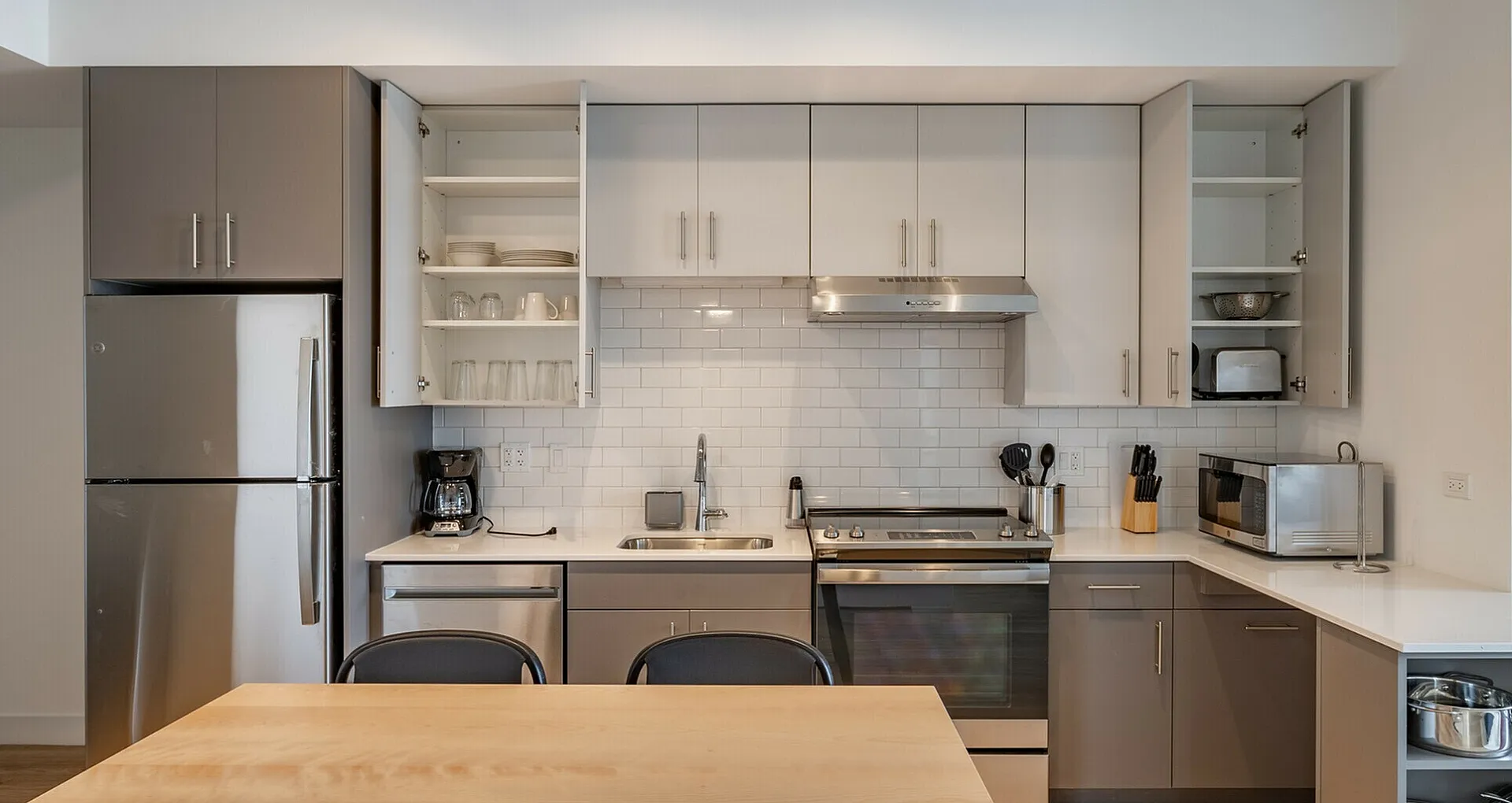 Modern kitchen with sleek stainless steel appliances, stylish cabinetry, and chic subway tile backsplash, featuring a wooden dining table and ample natural light.