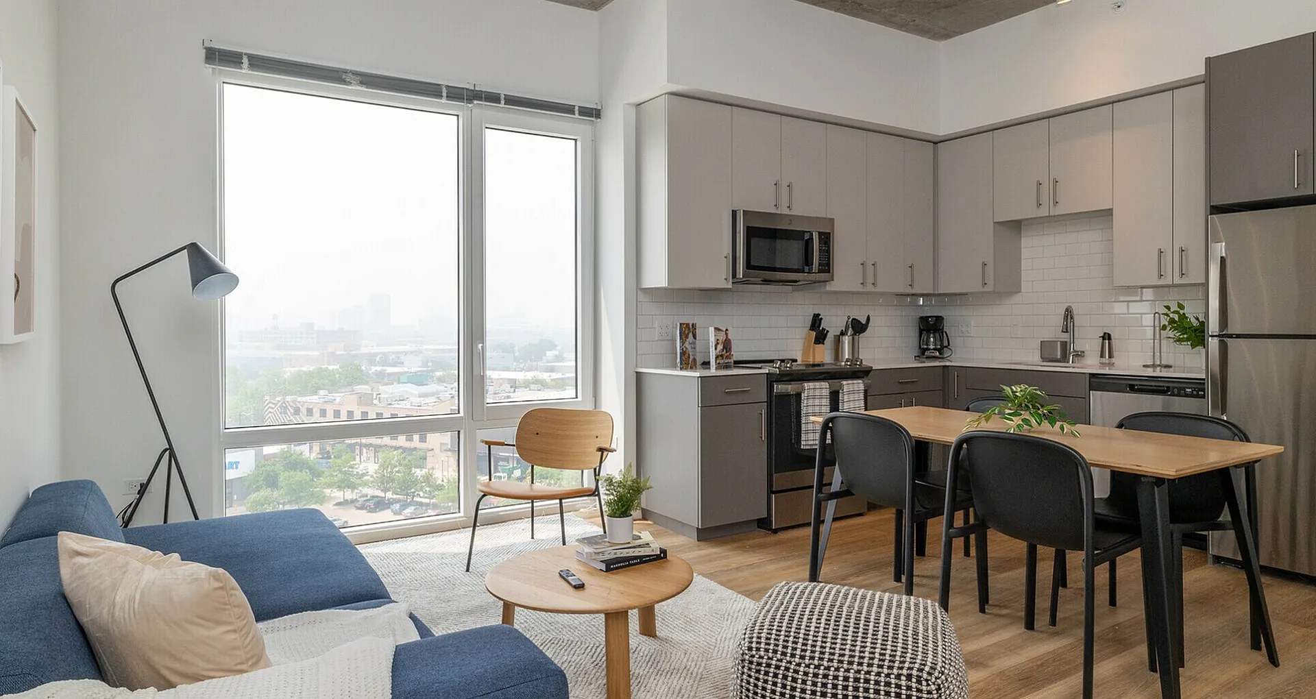 Modern open-plan living area with large windows showcasing stunning city views, sleek kitchen design, and cozy seating spaces.