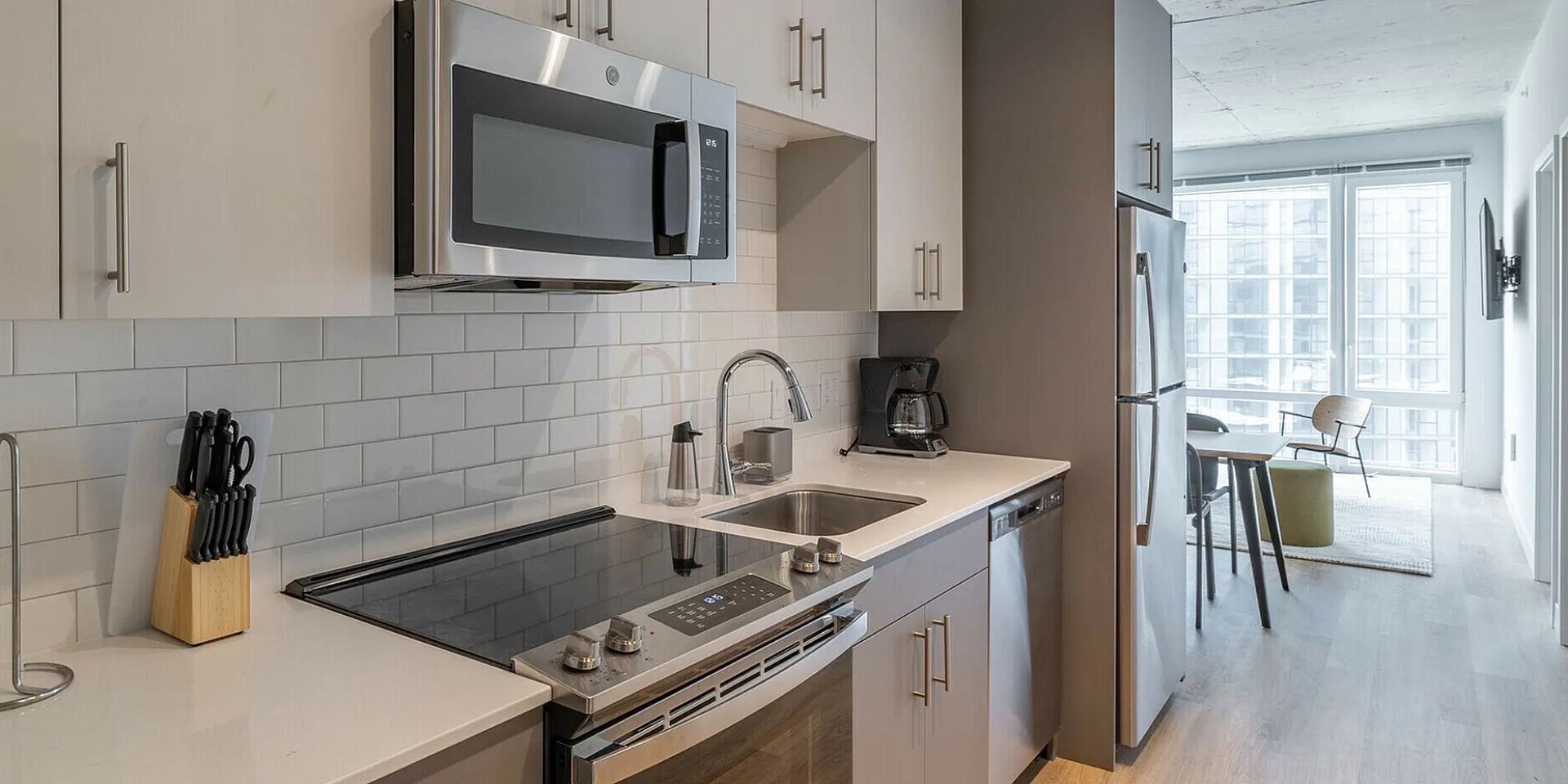 Modern kitchen with sleek stainless steel appliances, stylish cabinetry, and a sunlit dining area in a chic apartment.