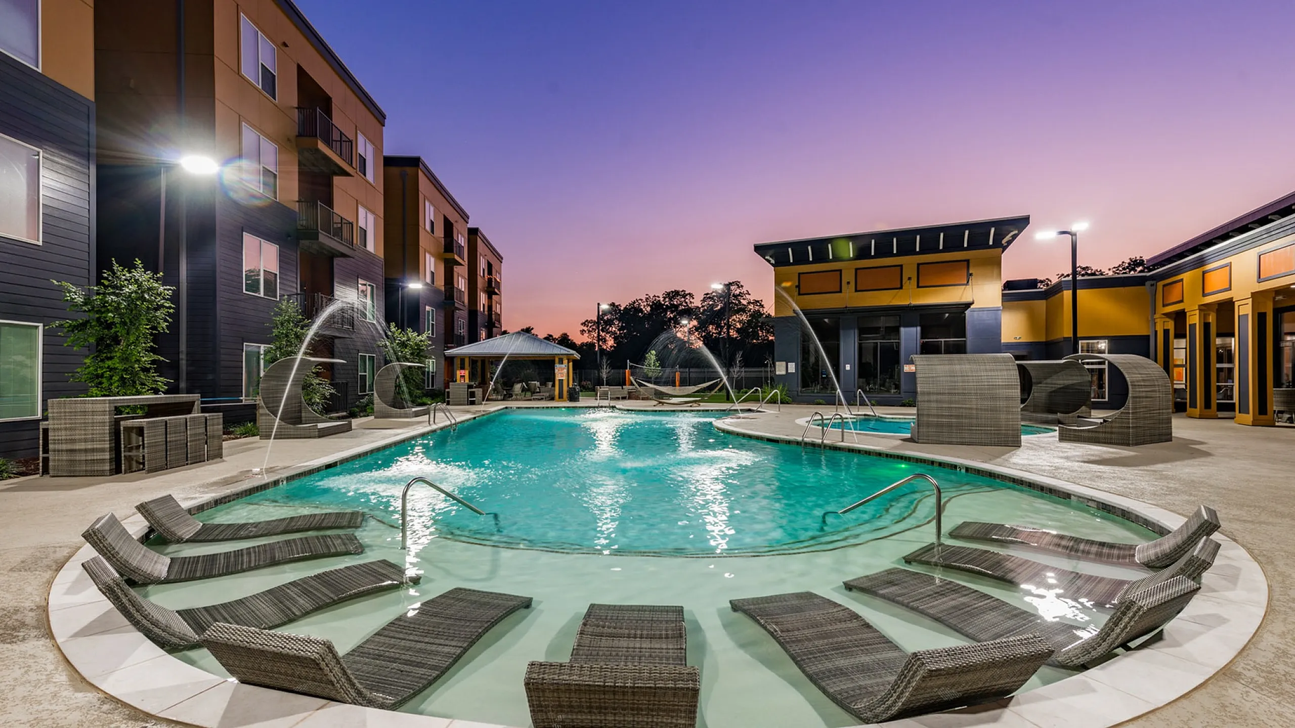 Luxurious apartment complex featuring a stunning pool with elegant lounge chairs at sunset, perfect for relaxation and leisure.