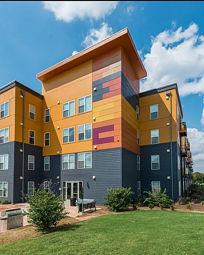Vibrant modern apartment complex with colorful exterior, spacious balconies, and lush green surroundings under a bright blue sky.