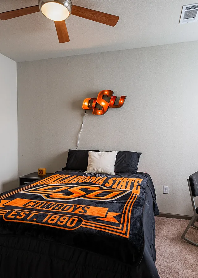 Cozy bedroom showcasing a stylish bed with themed bedding, modern ceiling fan, and convenient study desk by sunlight-filled window.