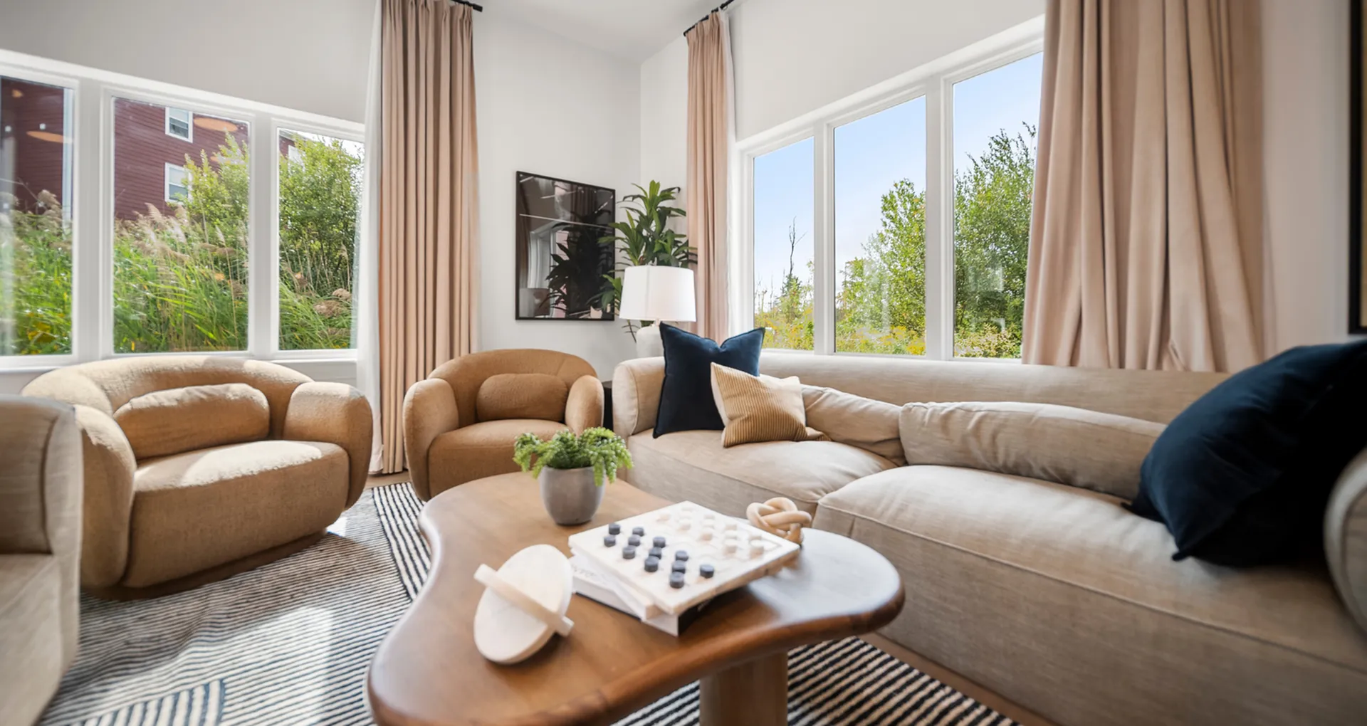 Bright and cozy living room with plush beige sofas, large windows offering lush garden views, and stylish decor accents.