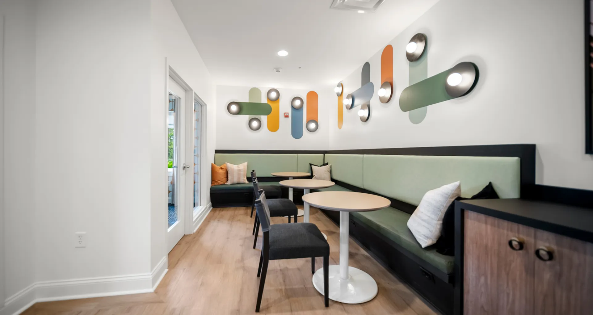 Chic modern seating area with colorful geometric wall lights, wooden flooring, and cozy banquette seating.