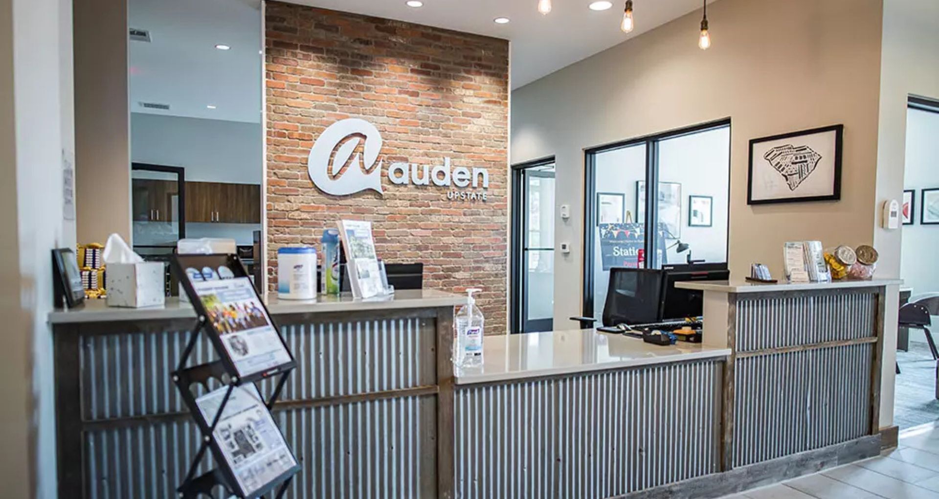Charming leasing office with rustic brick wall, sleek counter, and ambient lighting at Auden Upstate.