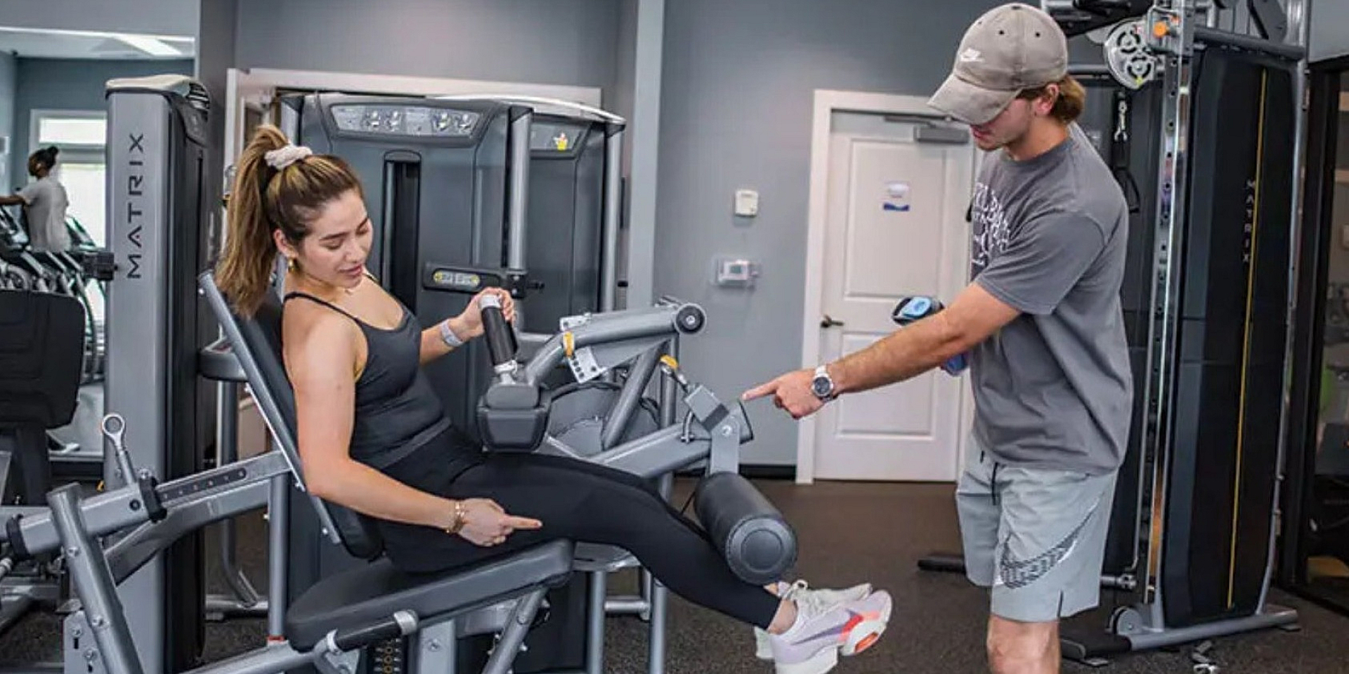Modern fitness center featuring a personal trainer assisting a woman on gym equipment, highlighting state-of-the-art facilities.