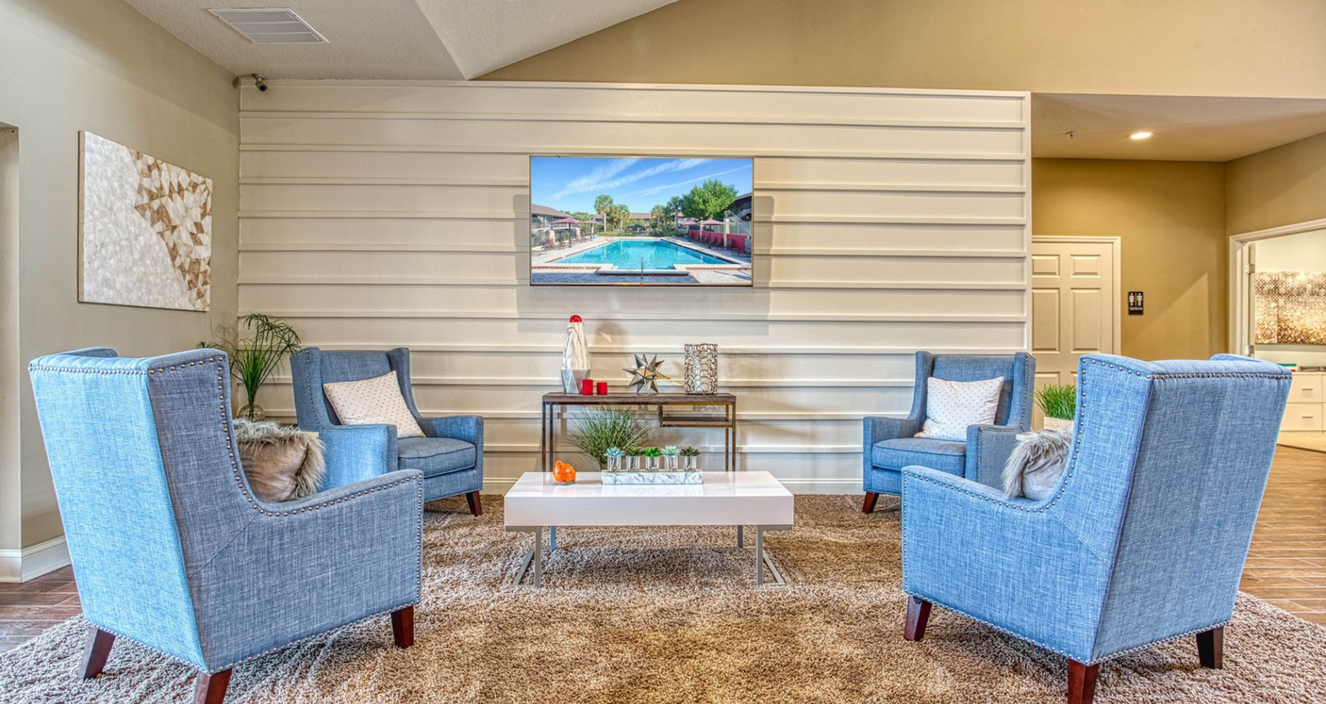 Inviting and elegant living room featuring stylish blue armchairs, a chic coffee table, and a wall-mounted TV displaying a serene pool view.